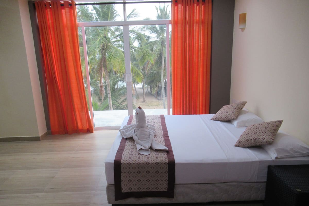 A hotel room with a large bed, orange curtains, and a view of palm trees.