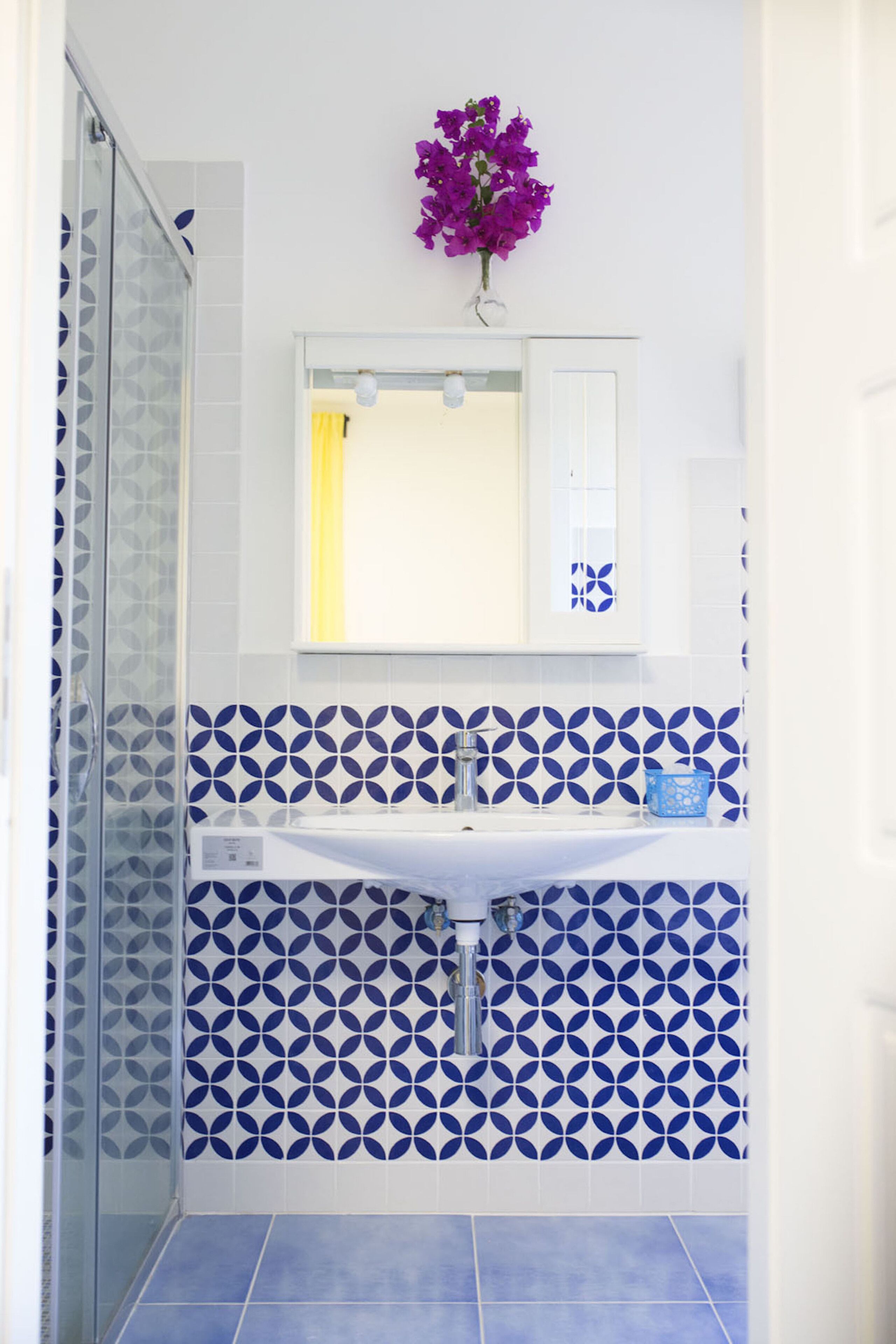 A bathroom with a glass shower enclosure, a white sink, and a blue and white patterned tile backsplash.