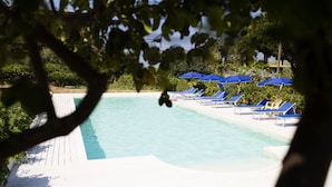 A pool area with blue umbrellas and sun loungers, surrounded by greenery. - B&B Il Cavaliere (Ricadi)