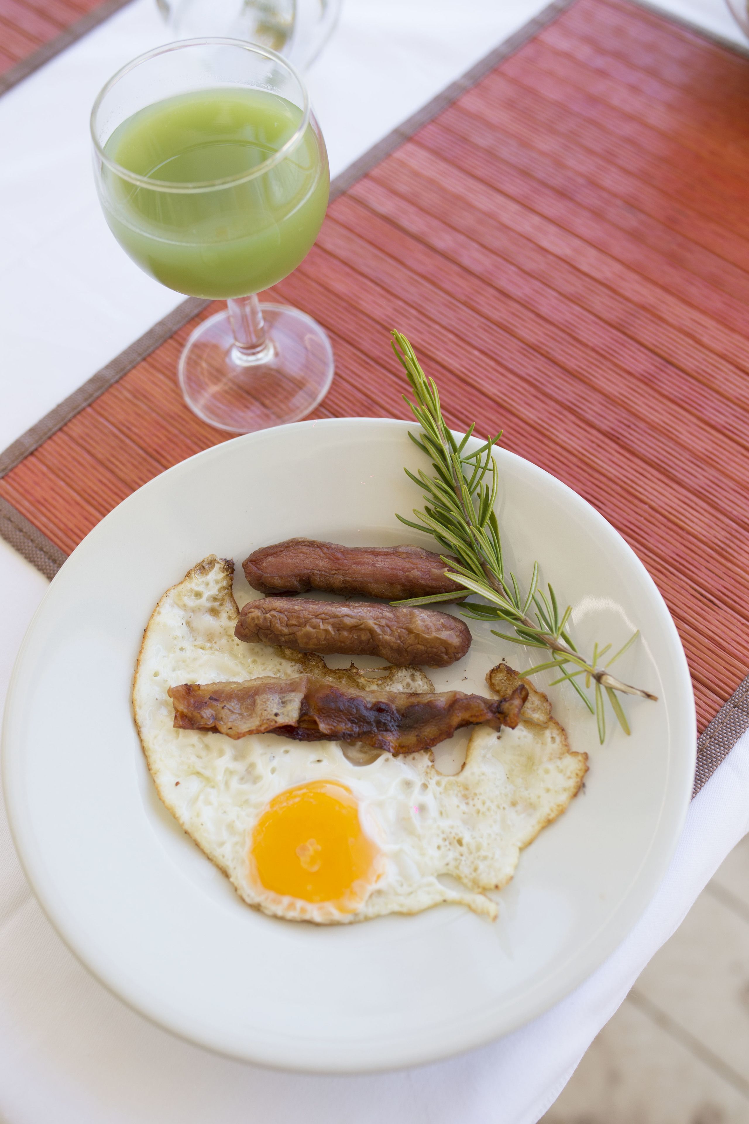 A plate with eggs, sausages, and a sprig of rosemary on a white plate.