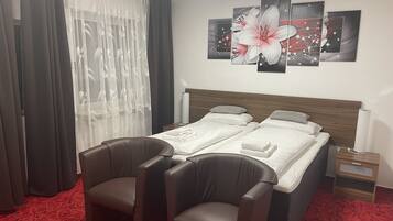 Habitación de hotel con dos camas, un ventanal con cortinas translúcidas, una alfombra roja y una pared decorada con tres cuadros.