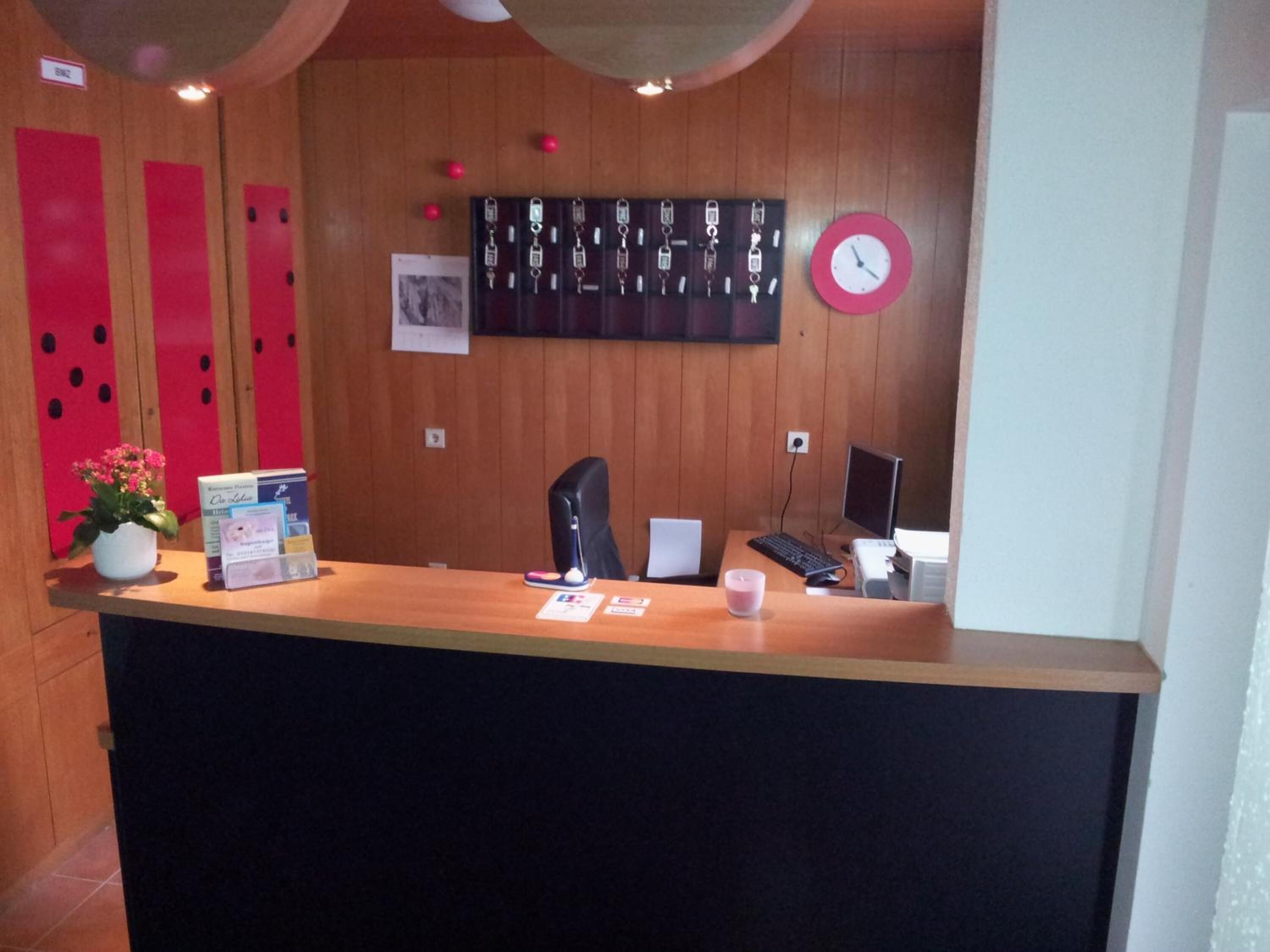 A reception desk with a clock, a computer, and a plant.