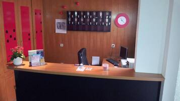 A reception desk with a clock, a computer, and a plant.