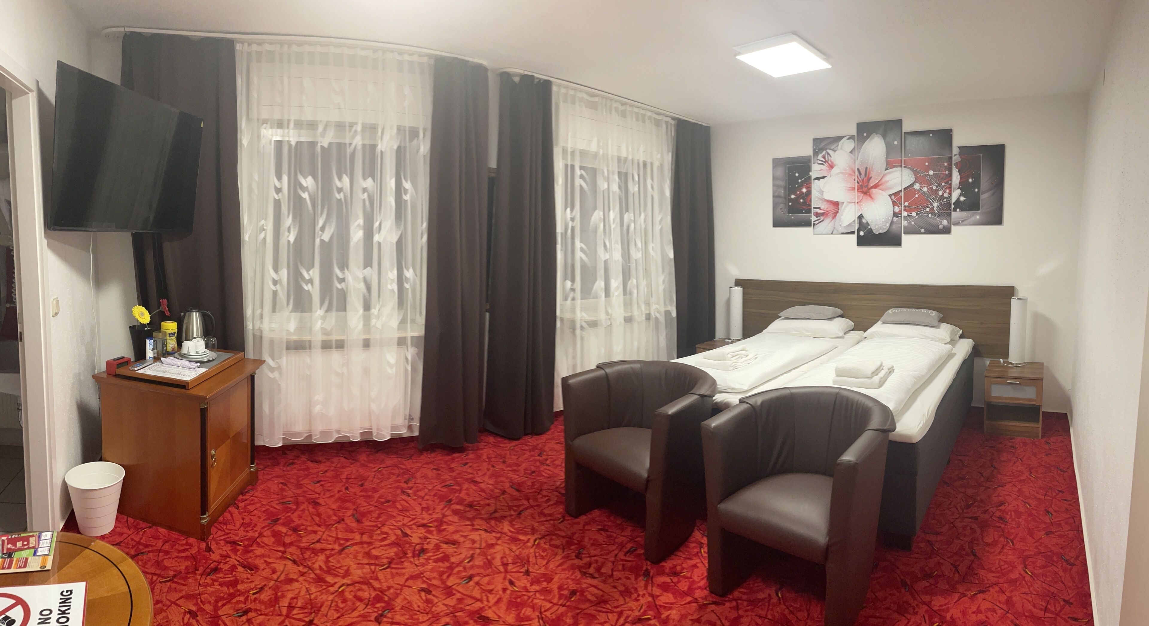 Habitación de hotel con cama, dos sillones, escritorio con televisión de pantalla plana, cafetera y alfombra roja.