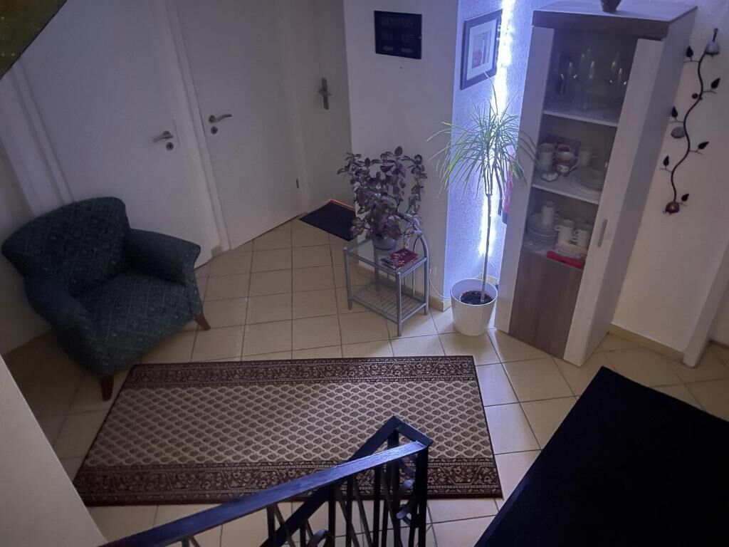 Una sala de estar con un sofá, una mesa de centro, una planta en maceta, un mueble con puertas de cristal y una escalera con barandilla.