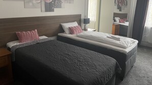 Habitación de hotel con dos camas, cabecera de madera, mesita de noche con lámpara y un espejo grande.