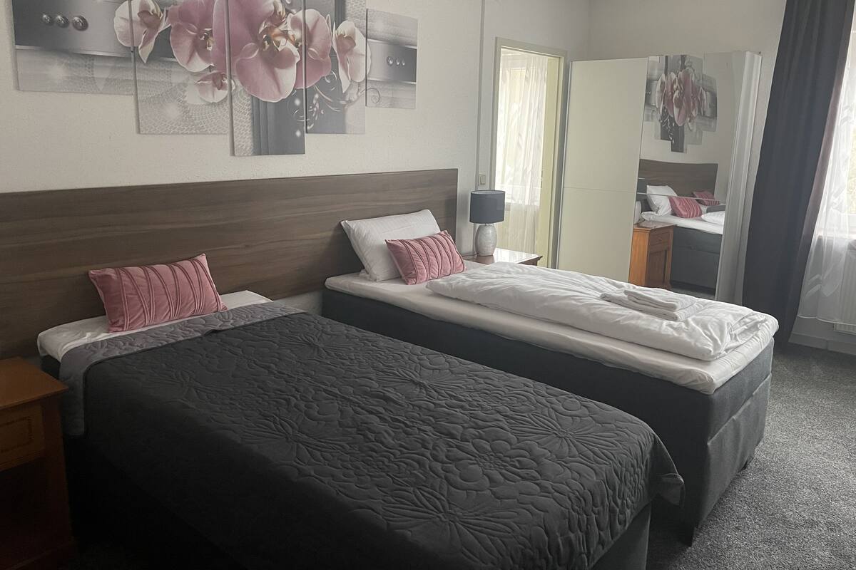 A hotel room with two beds, a wooden headboard, a nightstand with a lamp, and a large mirror.