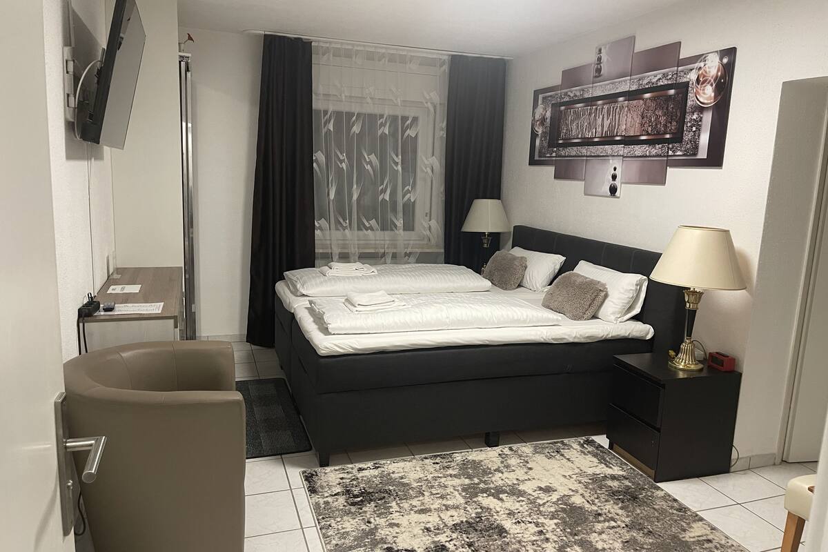 A hotel room with a bed, bedside tables, a desk, a chair, a rug, and a TV mounted on the wall.