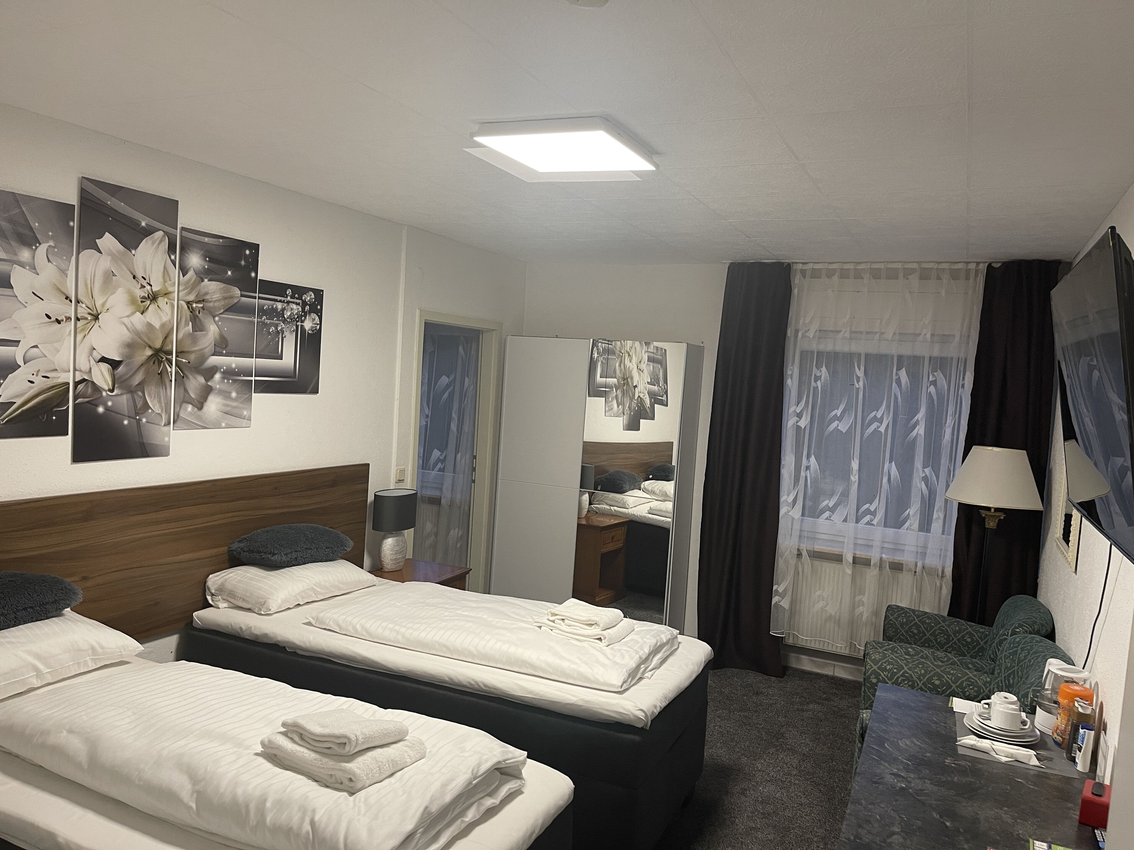 Habitació d'hotel amb dos llits, un escriptori, una cadira, un televisor i una finestra amb cortines.