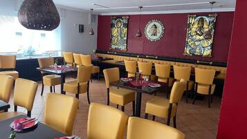 Un restaurante con sillas y mesas amarillas, una pared roja con obras de arte y una lámpara colgante.