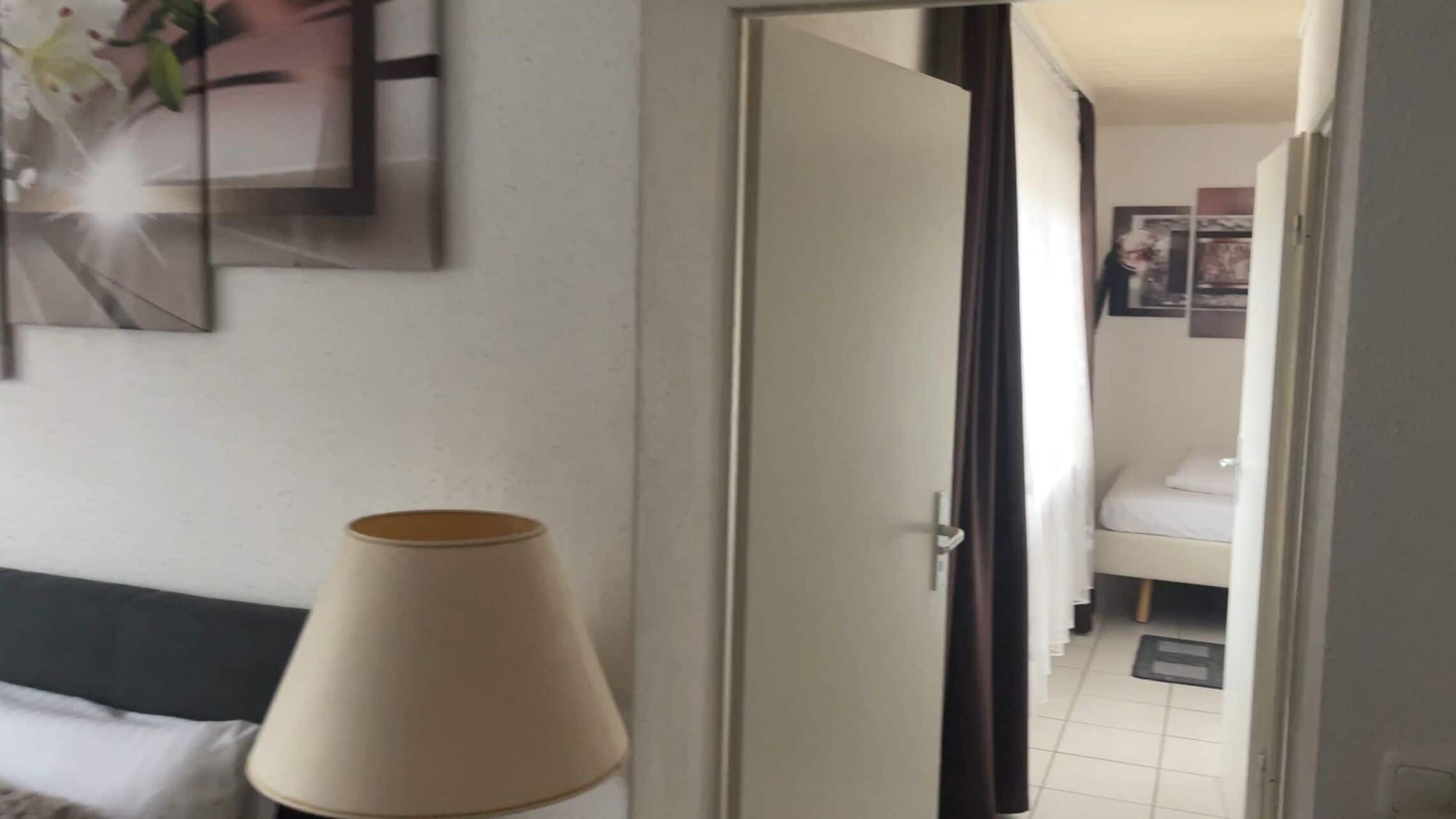 A hotel room with a bed, a lamp, and a door leading to another room.