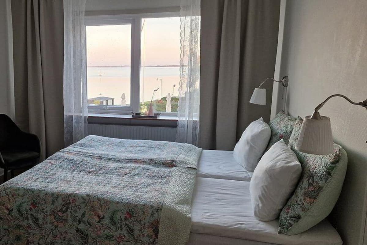 Habitación de hotel con cama, escritorio, silla, lámpara y vista al mar.