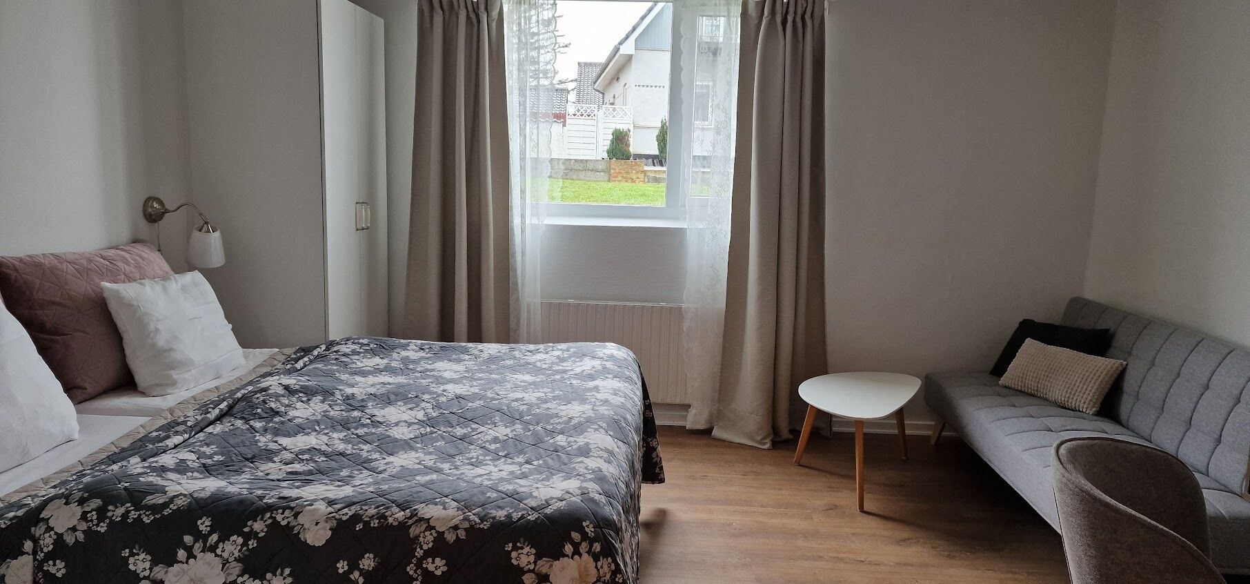 Une chambre à coucher avec un lit, un canapé, une petite table et une fenêtre avec des rideaux.