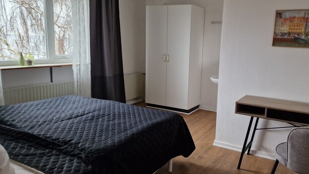 A bedroom with a bed, a wardrobe, a desk, and a chair. - Hotel Udsigten Marstal (Marstal)