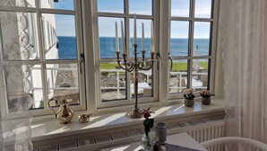 A room with a large window overlooking the sea, a candelabra, and a table with a vase of flowers. - Hotel Udsigten Marstal (Marstal)