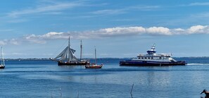 A ferry with a blue and white exterior, a sailboat, and a smaller boat in calm waters.