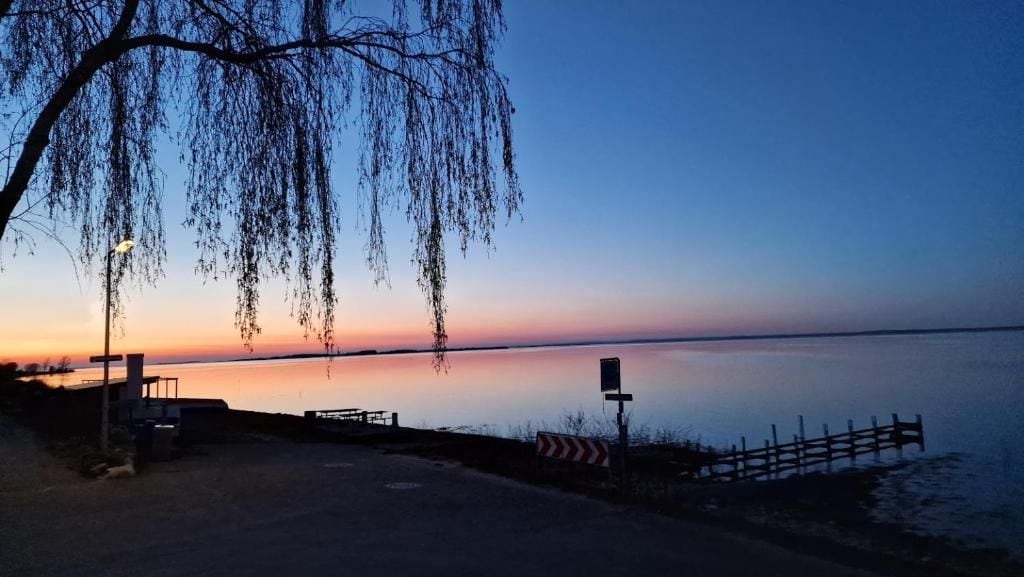Vista al agua con una superficie acuática tranquila, una cerca de madera y un camino que lleva a un área de embarcadero.