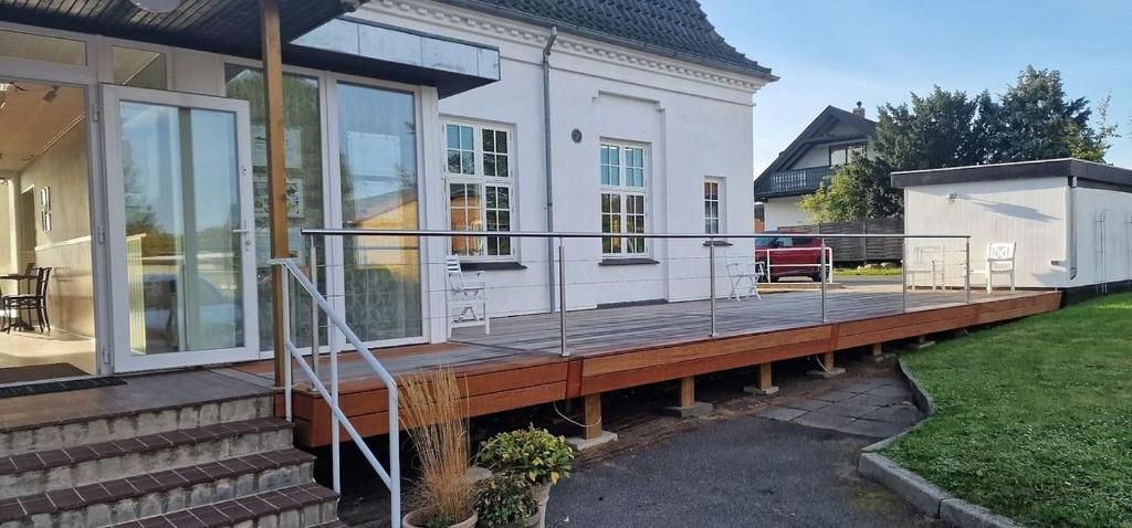 Ein weißes Haus mit einer Holzterrasse, einem Zugang durch eine Glastür und einem kleinen Garten.
