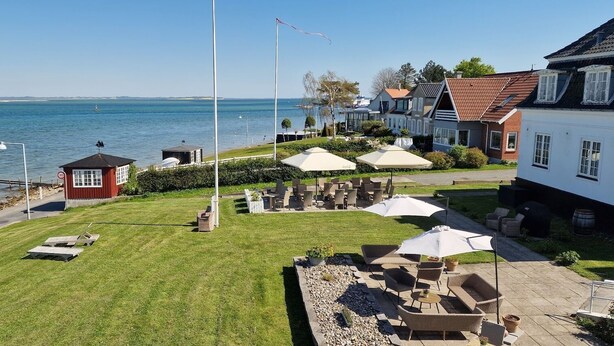 A coastal property with a grassy lawn, outdoor seating, and a view of the sea. - Hotel Udsigten Marstal (Marstal)