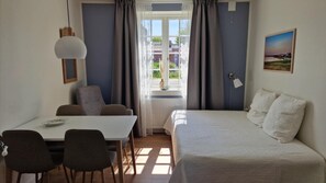 A bedroom with a bed, a table with chairs, a window with curtains, and a painting on the wall.