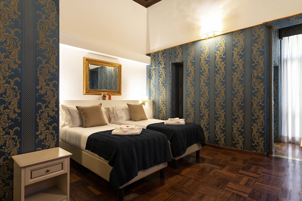 A hotel room with two beds, a nightstand, a mirror, and patterned wallpaper.
