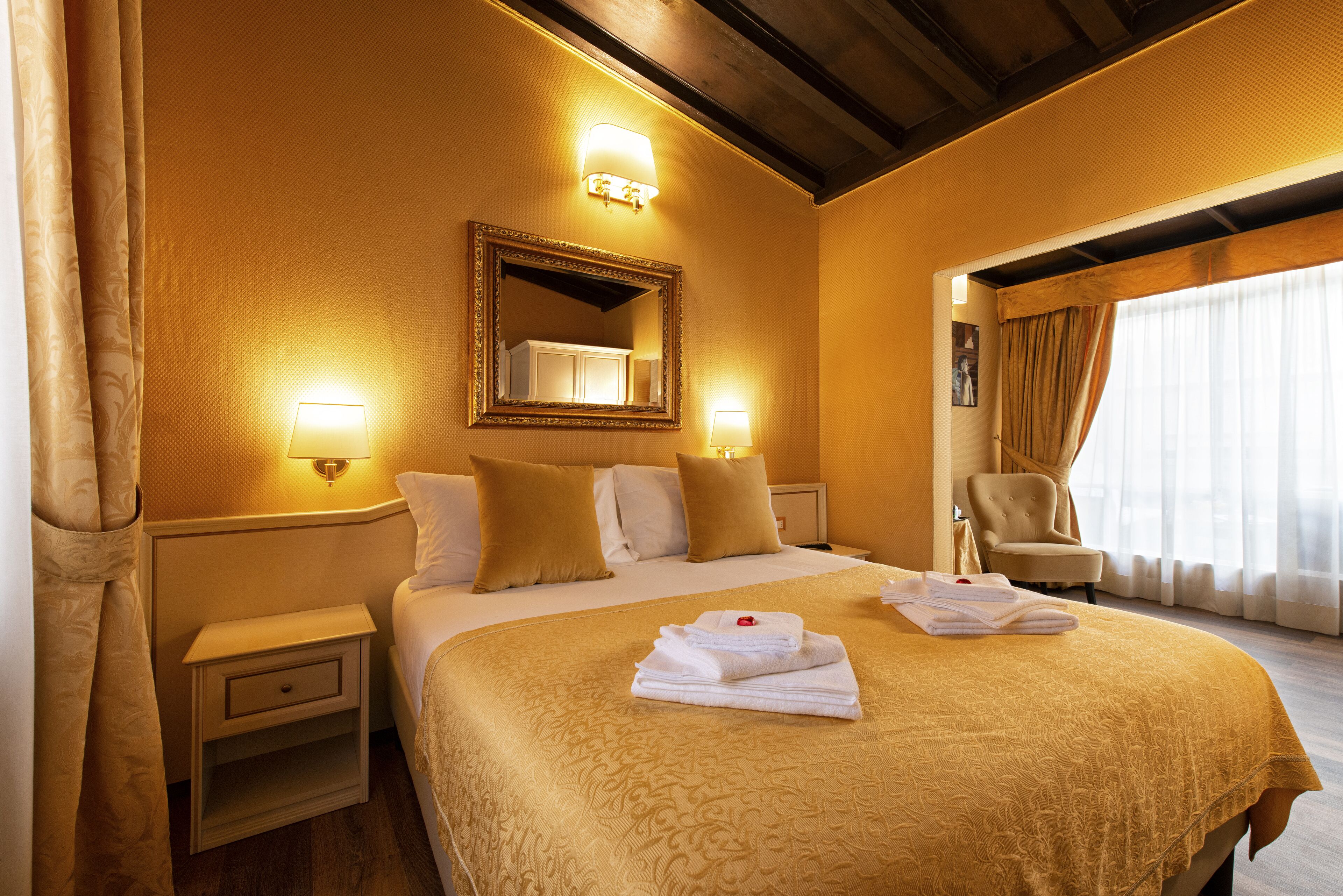 A hotel room with a large bed, two bedside lamps, a mirror, a chair, and a window with curtains.