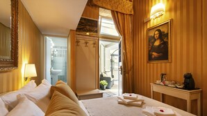 A hotel room with a bed, a painting, a desk with a coffee maker, and a view of the bathroom. - Canova Rooms in Spanish Steps (Rome)