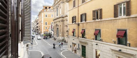 A street view of a historic urban area with buildings featuring classical architecture, cobblestone streets, and a mix of pedestrians and vehicles.