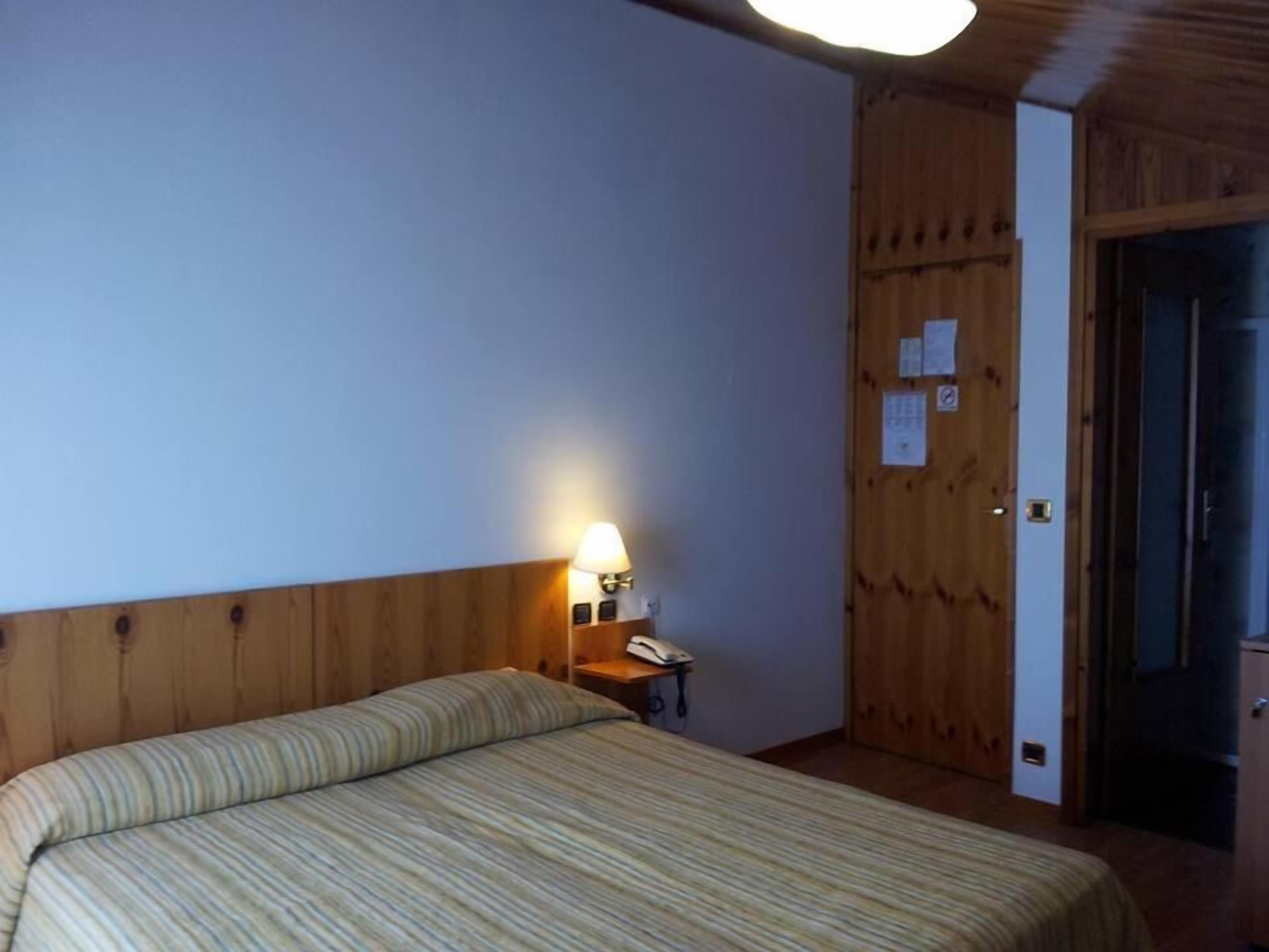Una camera d'albergo con un letto, un comodino, una lampada e un armadio in legno.