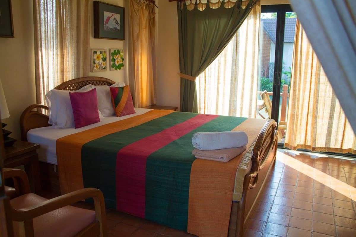 A neatly made bed with colorful bedding, a wooden headboard, and a view of the outdoors through a sliding door.