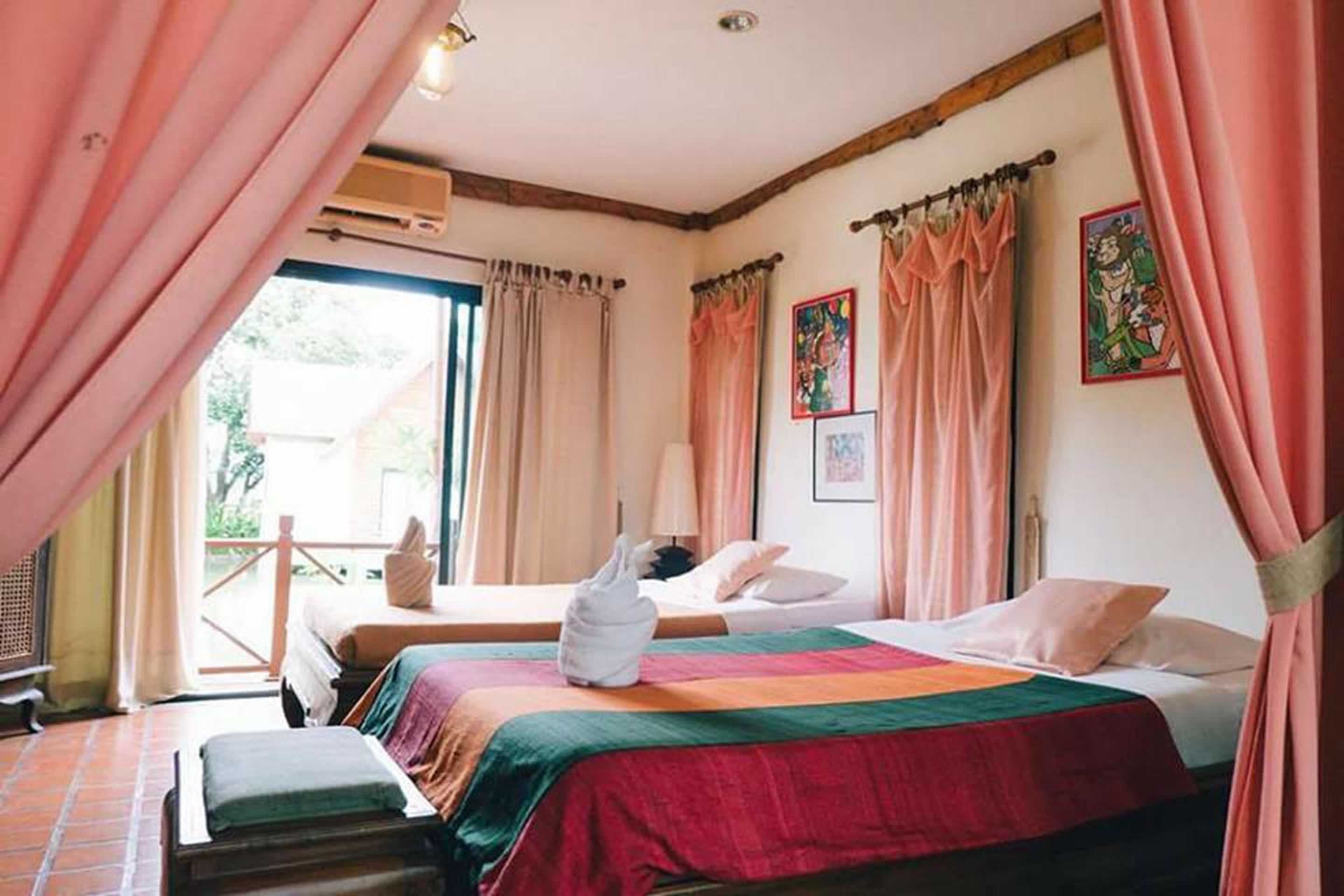 Une chambre avec deux lits, un banc et une vue sur l’extérieur.