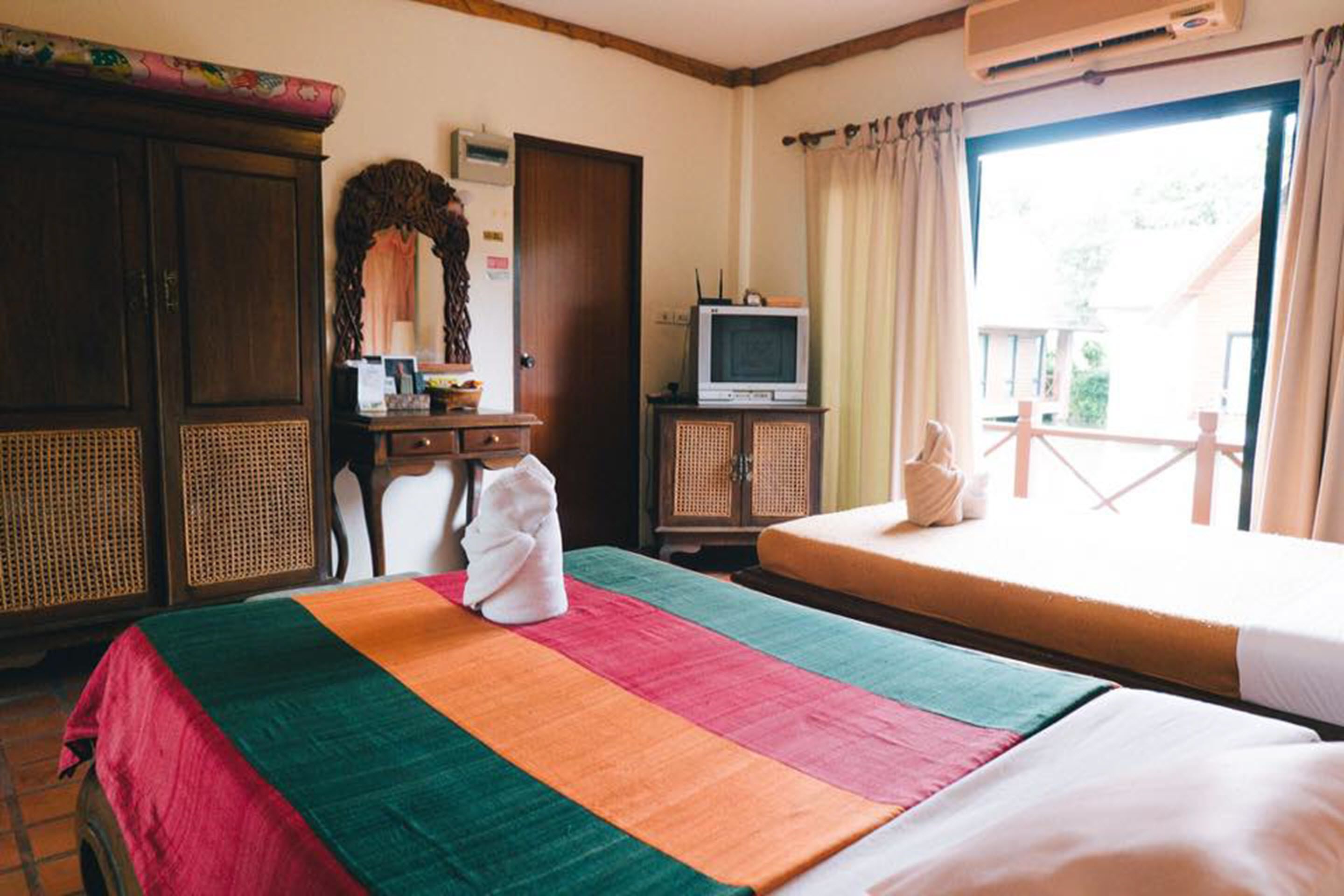 A hotel room with a bed, a desk with a television, a wardrobe, and a window with curtains.