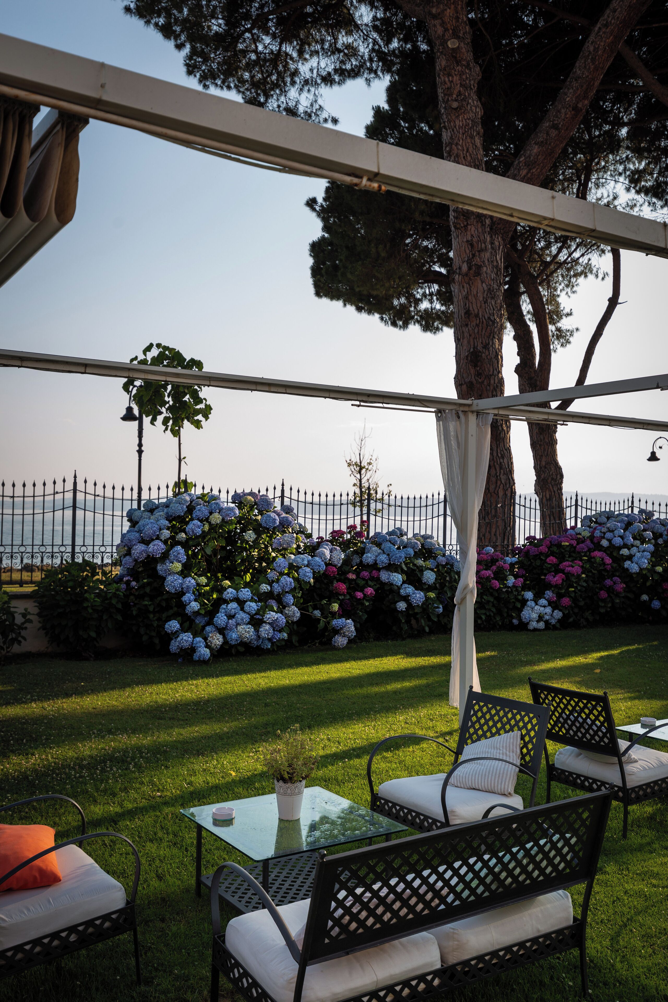 An outdoor seating area with tables and chairs, a pergola, and a view of the sea.