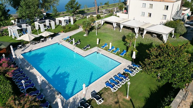 A hotel with a swimming pool, lounge chairs, and a view of the sea. - Hotel Holiday (Bolsena)