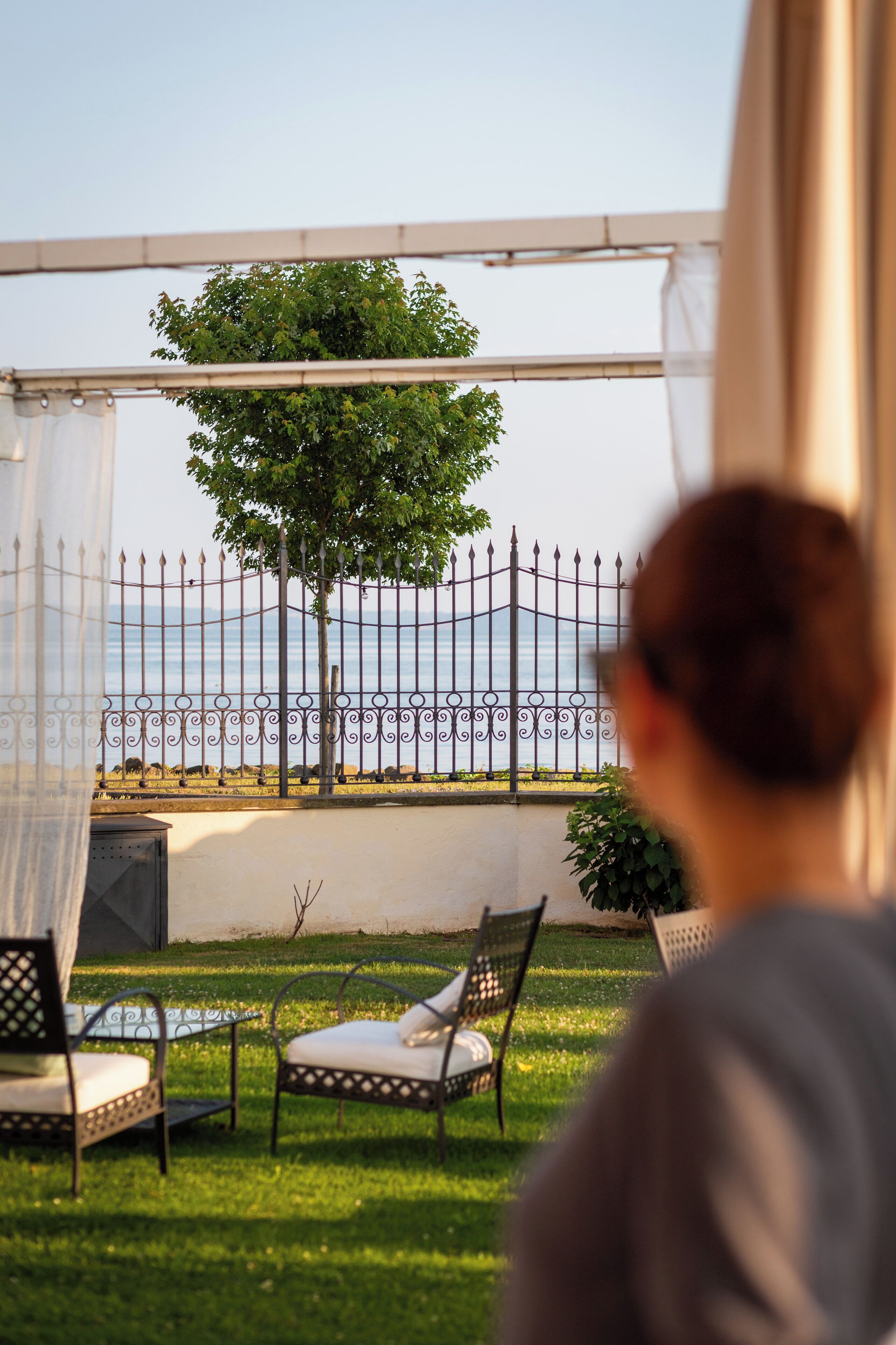 Un área de estar al aire libre con sillas, una mesa, una valla metálica y un árbol al fondo.