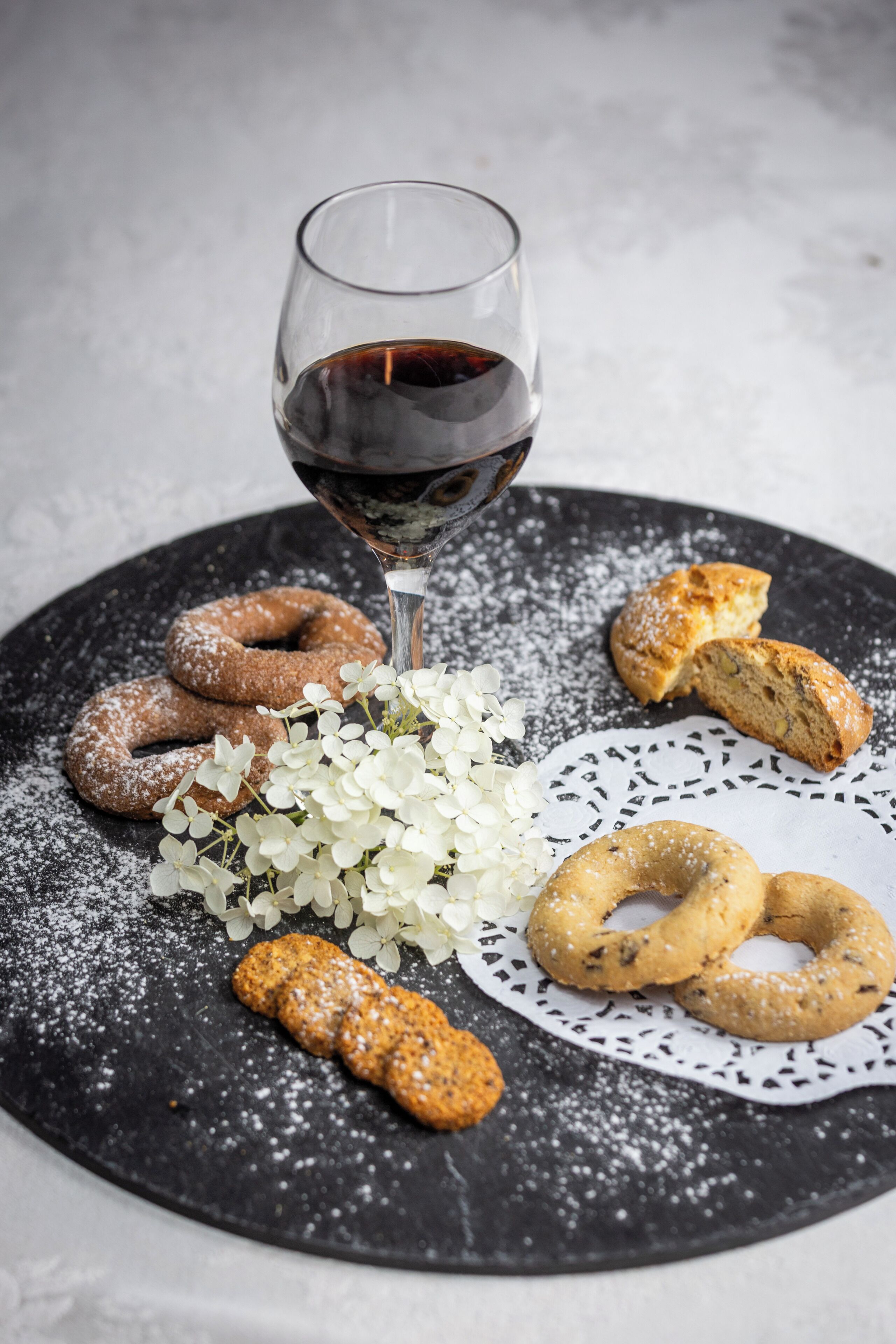 Un piatto con dolci e un bicchiere di vino rosso su una superficie nera strutturata.