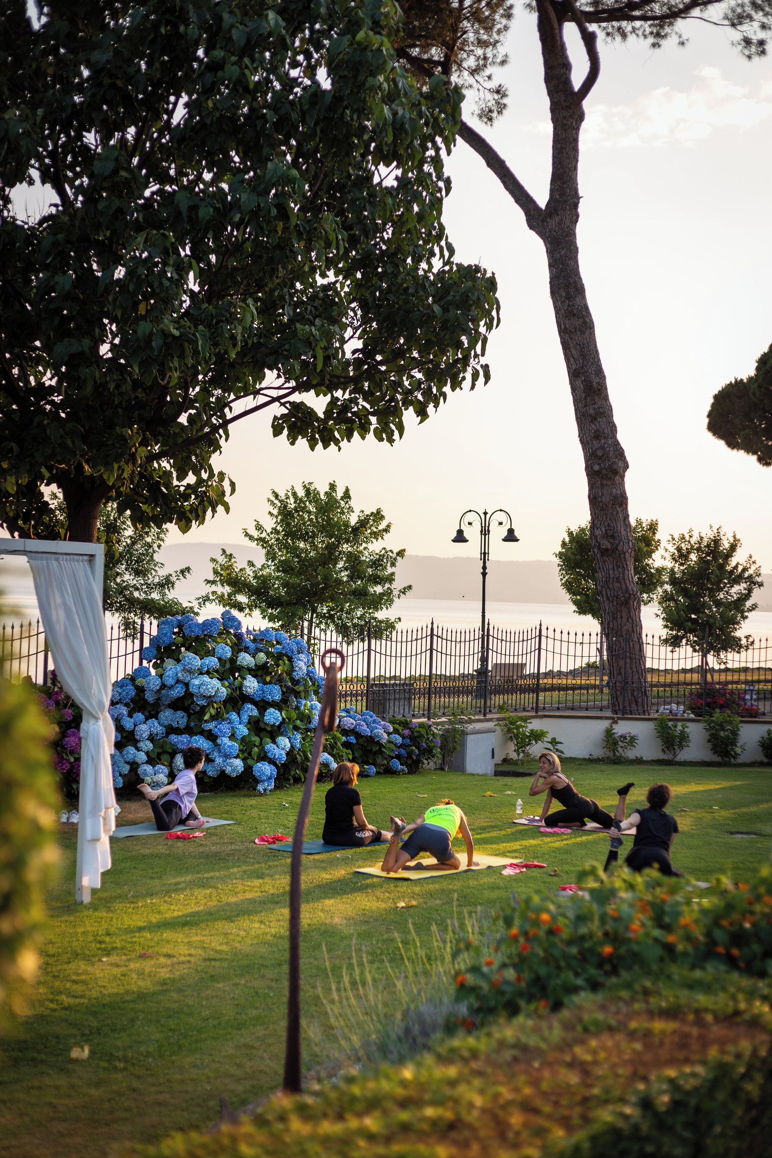 A group of people doing yoga on a grassy area with a view of the sea and a decorative blue flower arrangement.