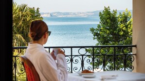 A person seated at a table on a balcony overlooking a body of water, with greenery and a clear sky in the background. - Hotel Holiday (Bolsena)