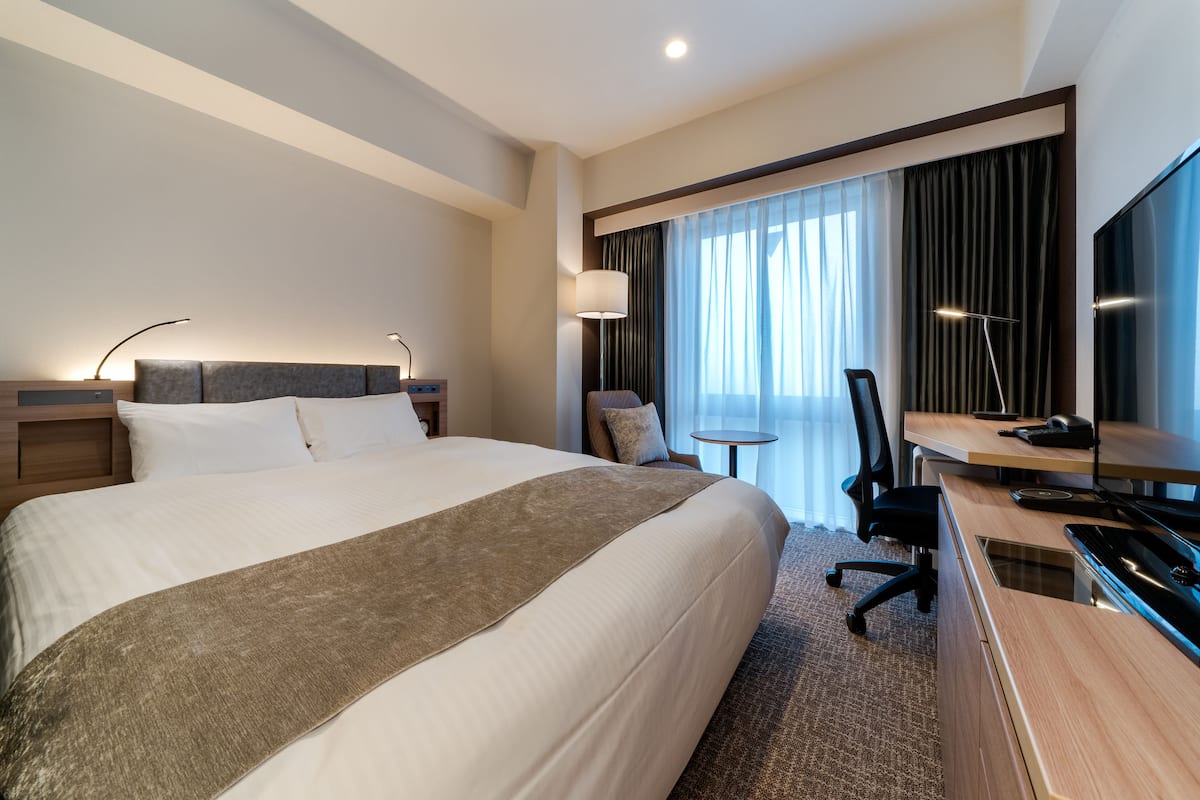 A hotel room with a large bed, a desk with a computer, a chair, and a TV.