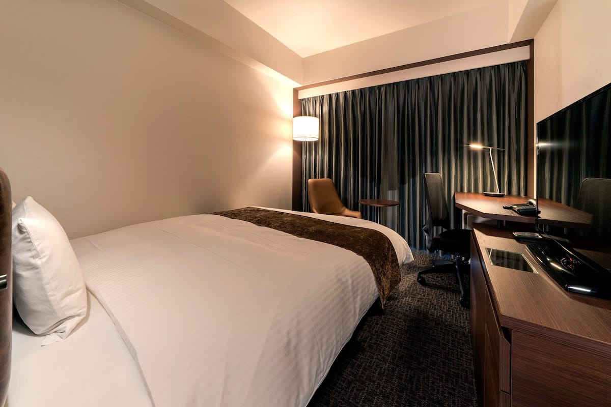 A hotel room with a large bed, a desk with a telephone, a chair, and a lamp.