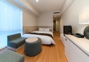 Una habitación de hotel moderna con una cama, un sofá, un taburete redondo, un escritorio con teléfono y una televisión.