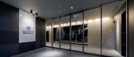 Entrada moderna de hotel com portas de vidro, uma placa indicando Hotel Daiwa Roynet e piso de azulejos.