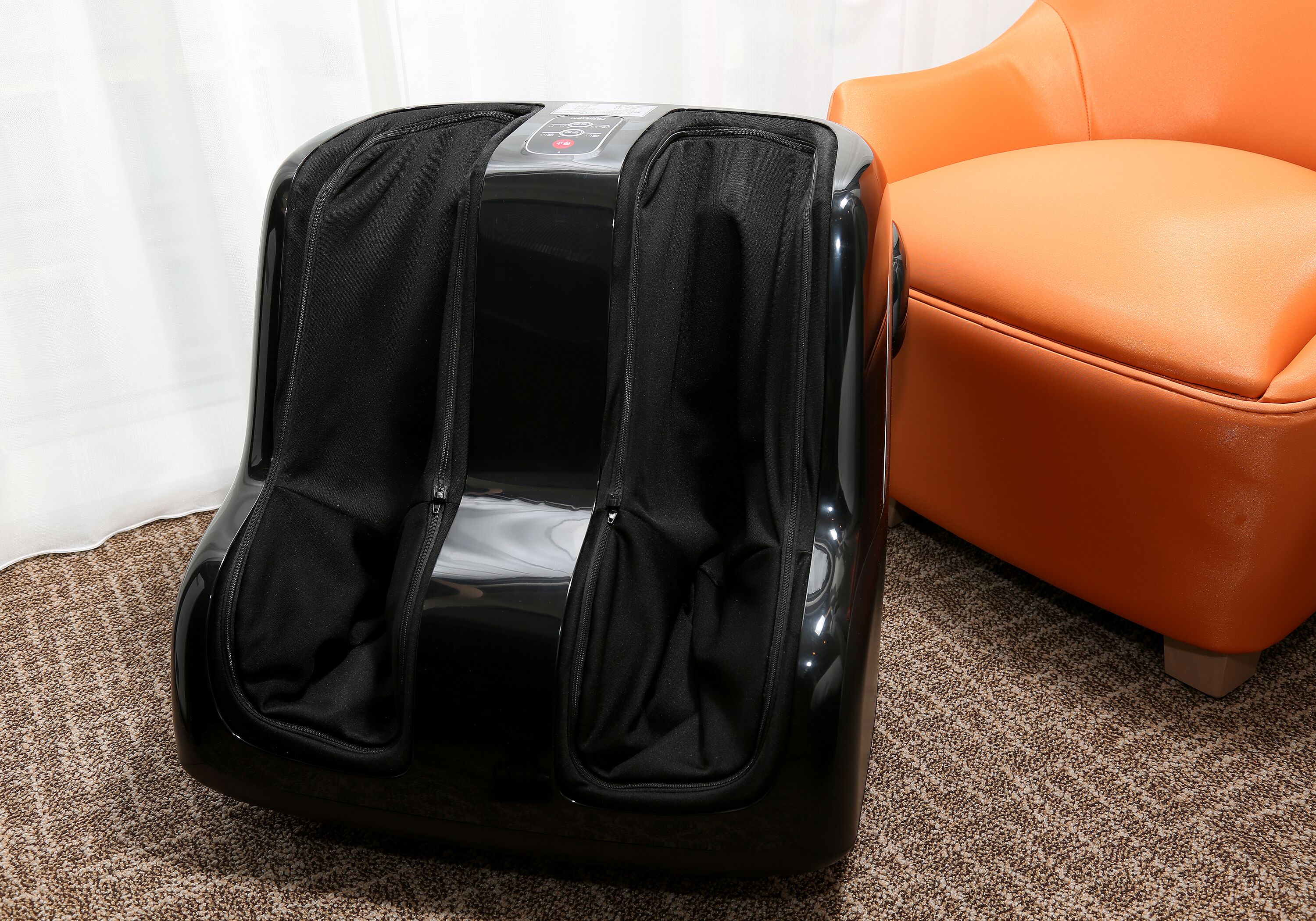 Una silla de masaje con un panel de control, ubicada al lado de una silla naranja.