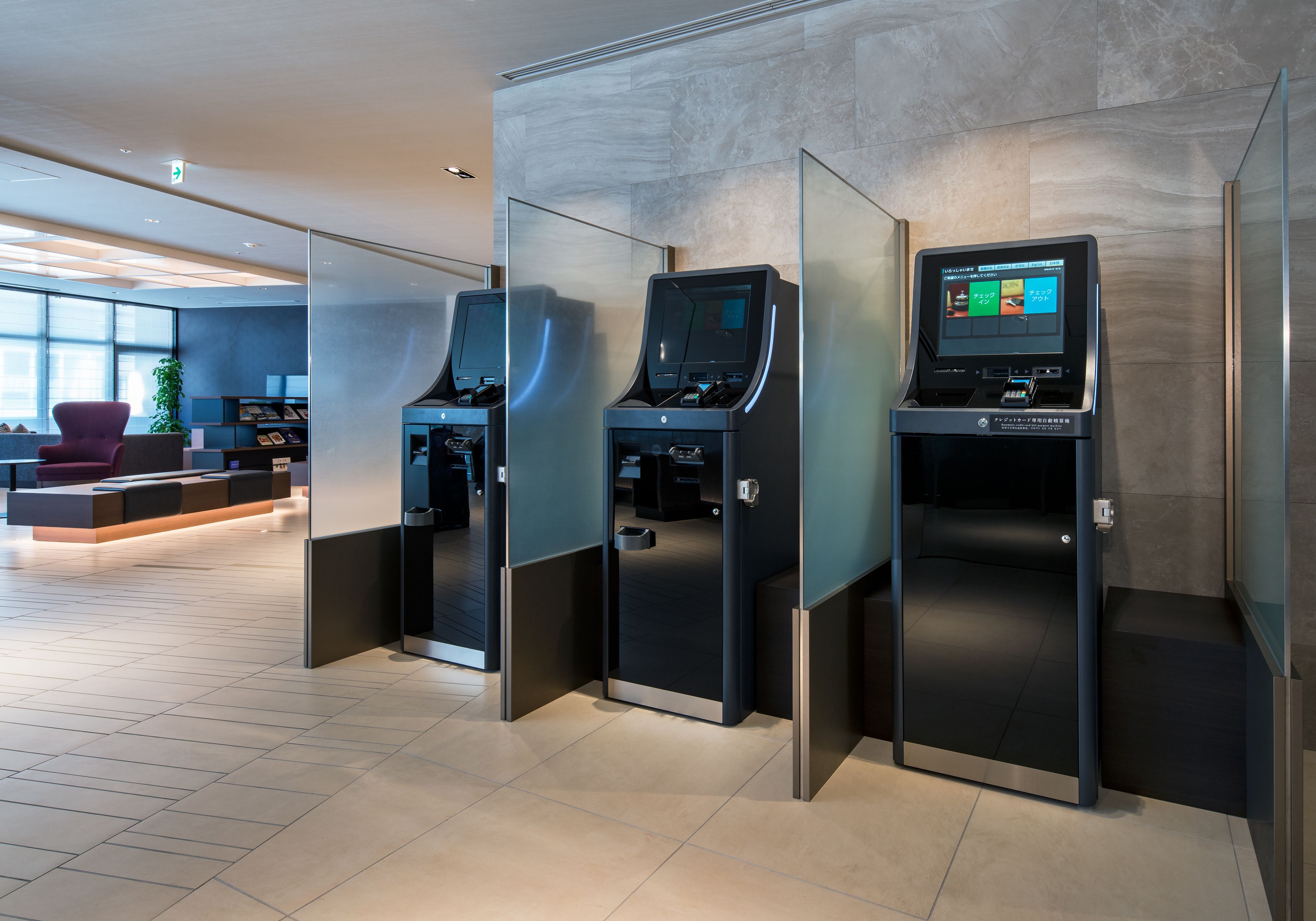 A modern hotel lobby with self-service kiosks, a seating area, and a large window providing natural light.