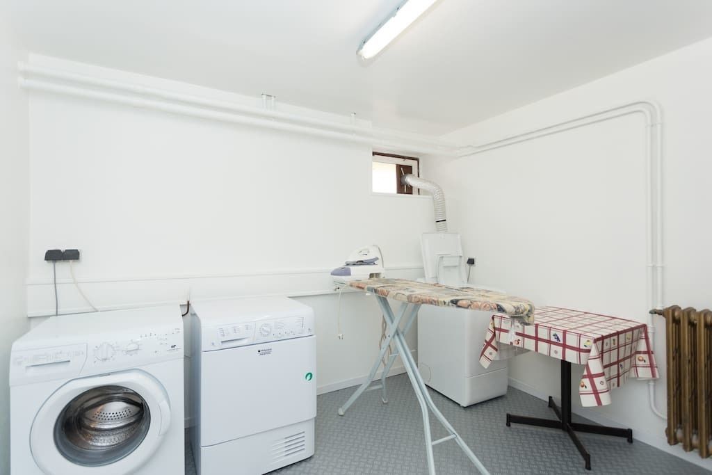 A laundry room with a washing machine, dryer, ironing station, and a radiator.