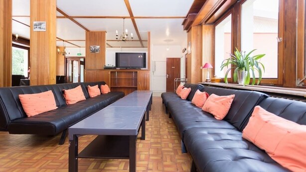 A hotel lobby with black leather sofas, a wooden reception desk, and a television. - Les Sources (Bussang)