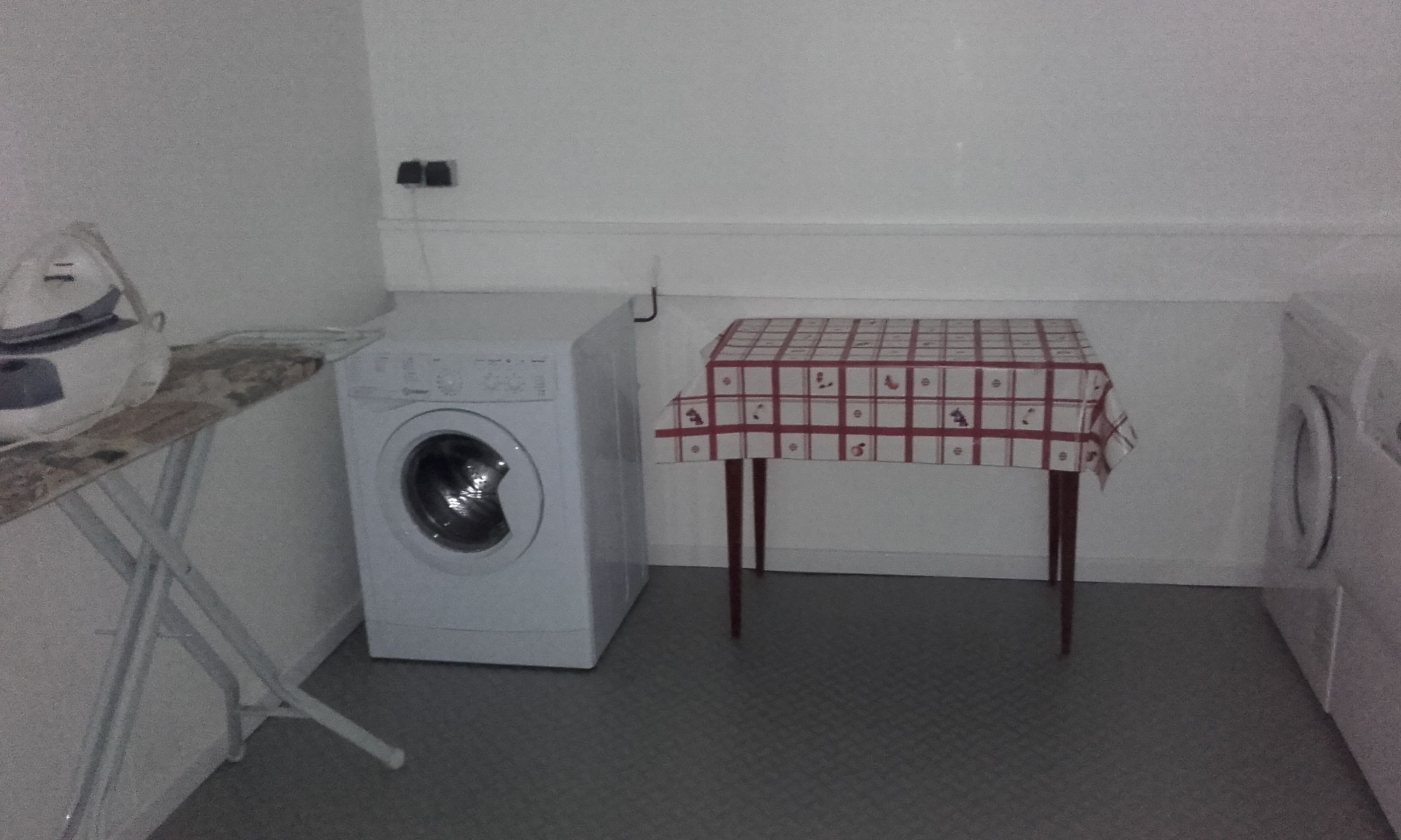 A laundry room with a washing machine, a table with a checkered tablecloth, and an iron on a counter.