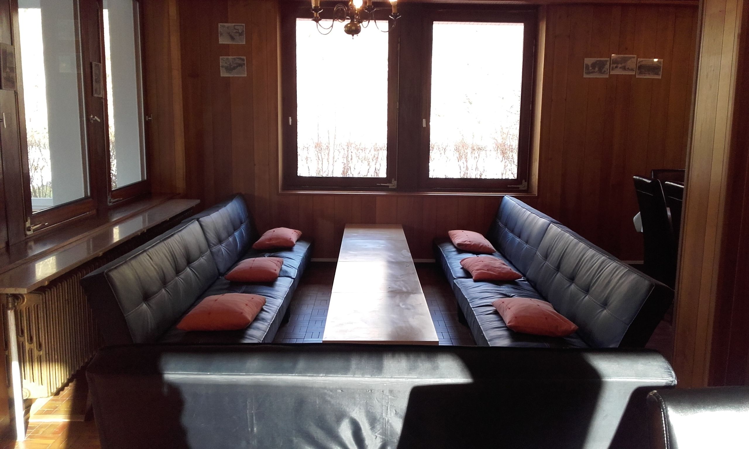Une pièce avec deux canapés en cuir placés face à face, une table en bois au centre et de grandes fenêtres donnant sur la forêt.