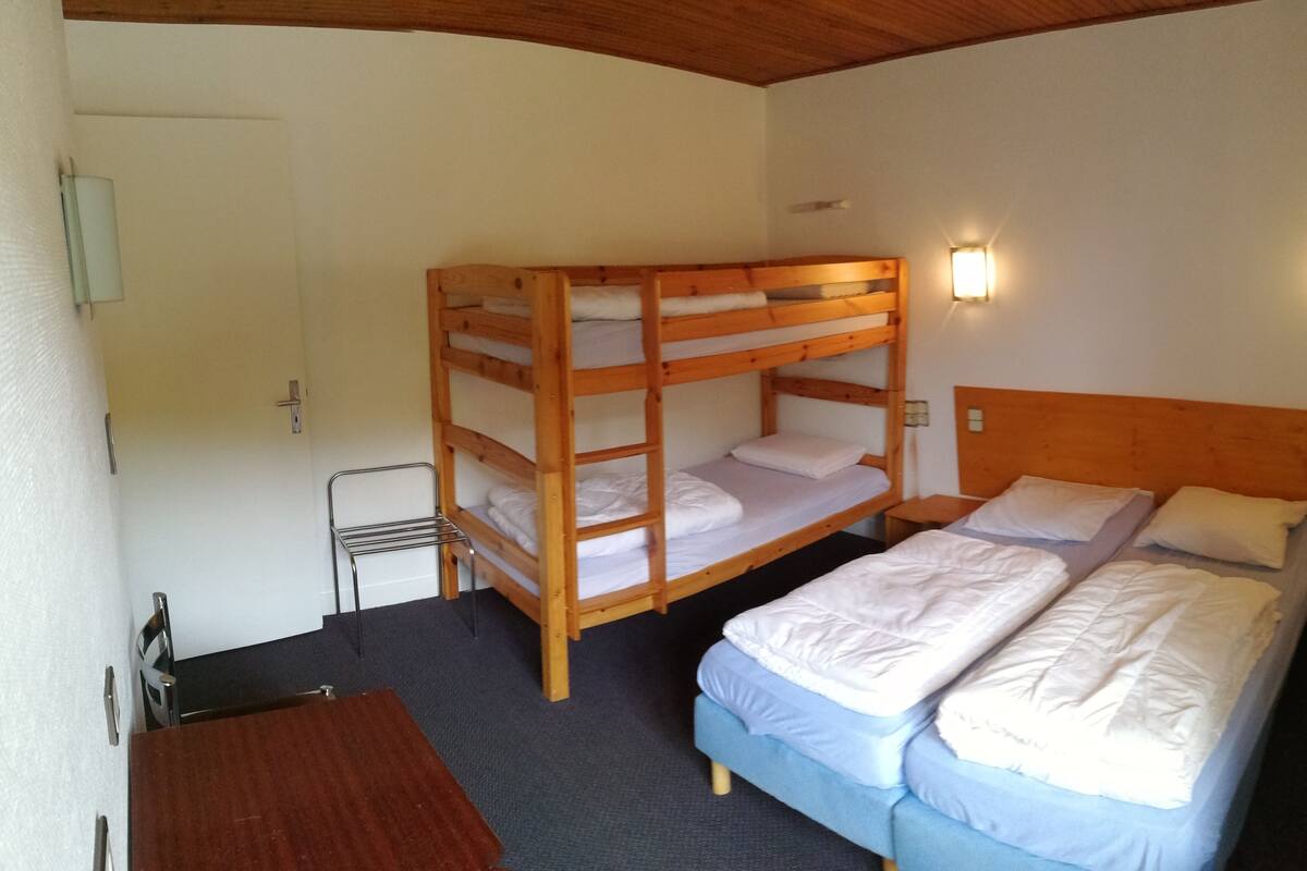 A bunk bed room with a wooden headboard, a small table, and a wall-mounted light fixture.