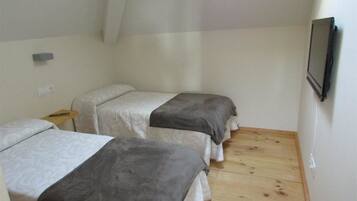 Une petite chambre, de taille modeste, avec deux lits simples, un plancher en bois, un téléviseur fixé au mur et une petite table avec une lampe.
